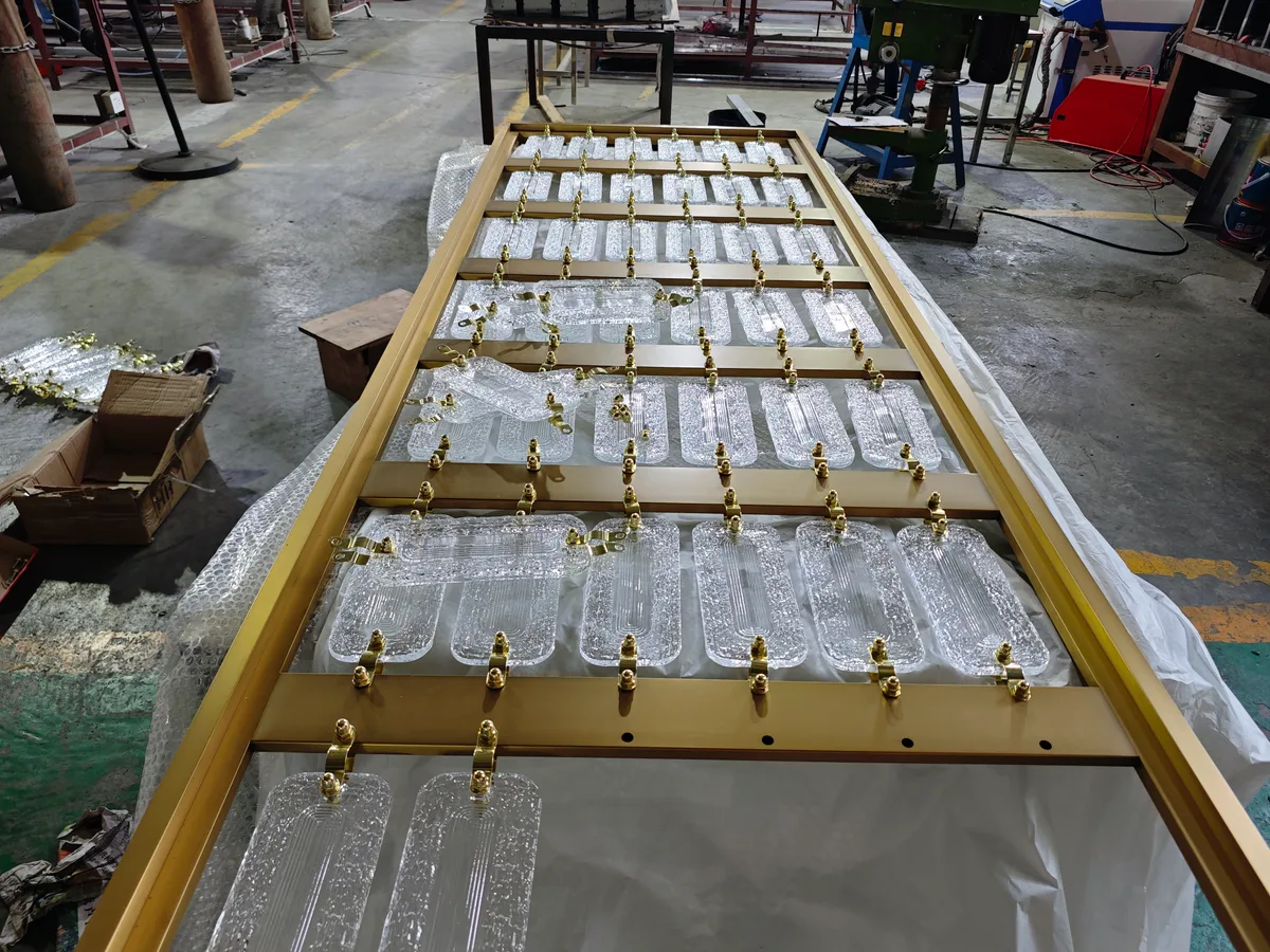 Clear rectangular textured crystal pieces linked in rows within a gold-colored frame lying on a workshop table.